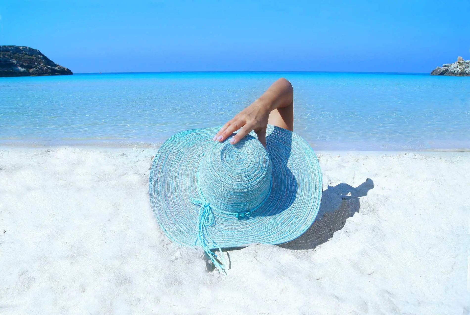 A person sitting on the beach with a hat in their hand.