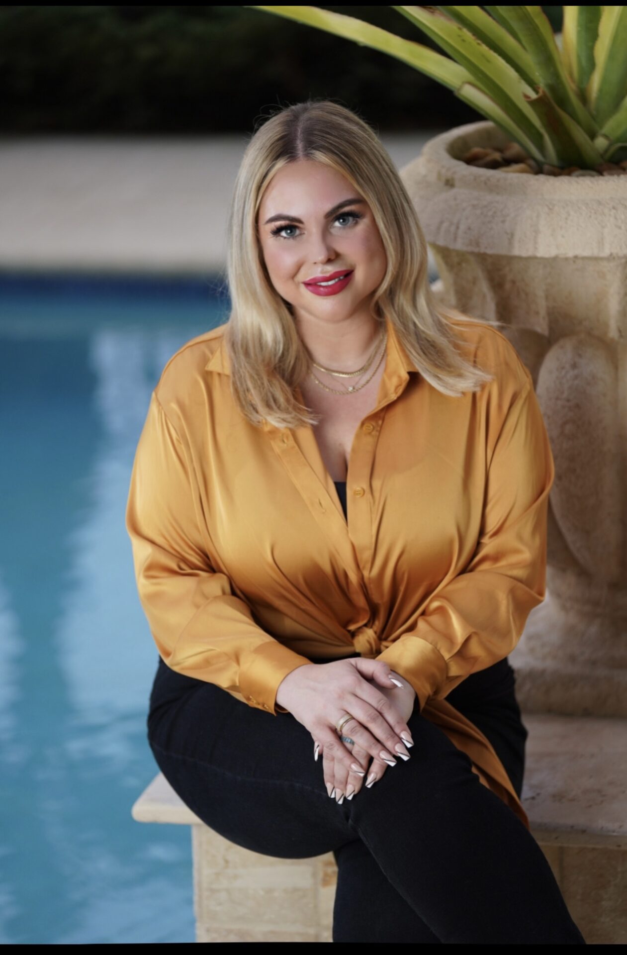 A woman sitting in front of a pool wearing an orange shirt.