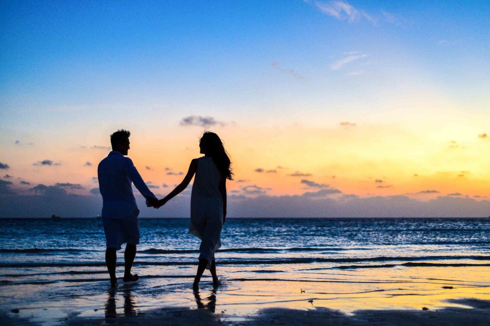 A man and woman holding hands on the beach.