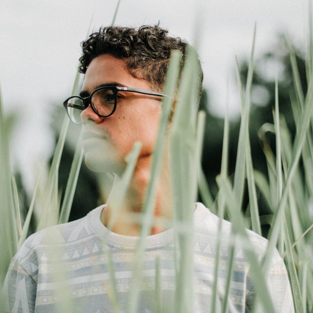 A man with glasses standing in tall grass.