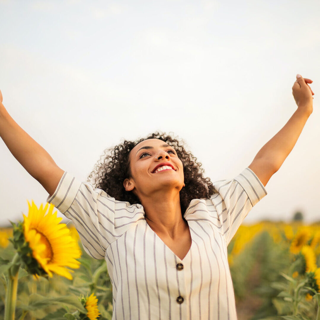 A woman standing in the middle of a field with her arms raised.