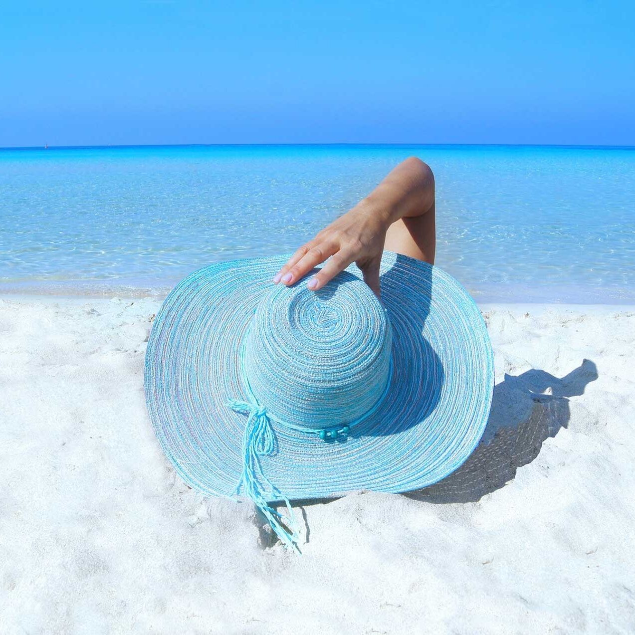 A person sitting on the beach with a hat in their hand.