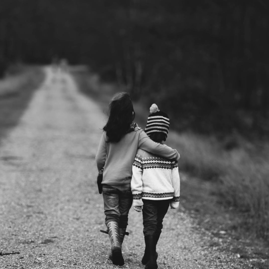 Two children walking down a dirt road.