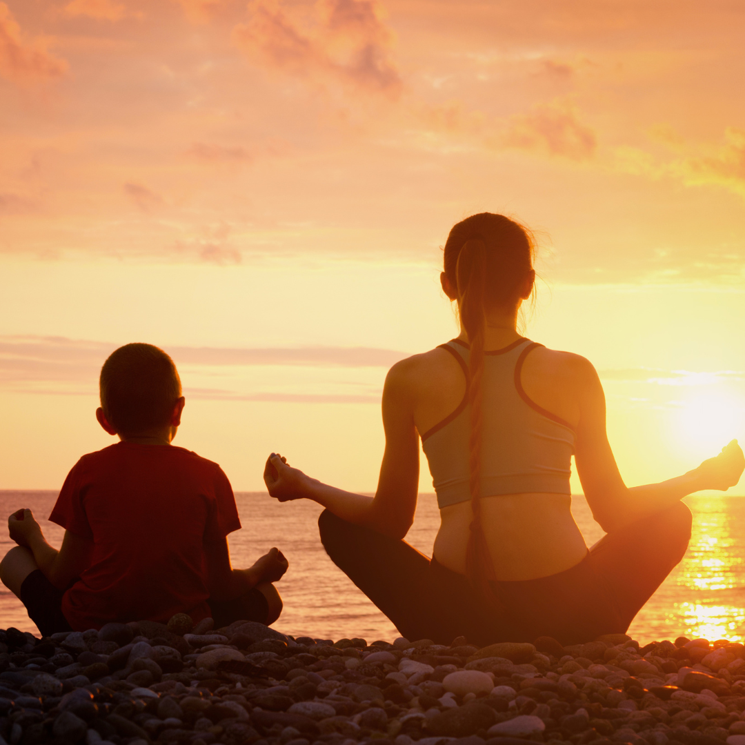 A woman and child sitting on the beach at sunset.