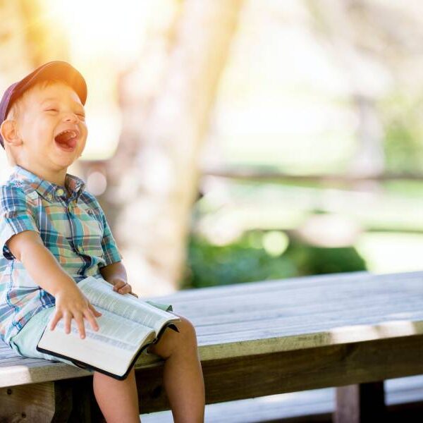 A little boy sitting on top of a bench holding an open book.