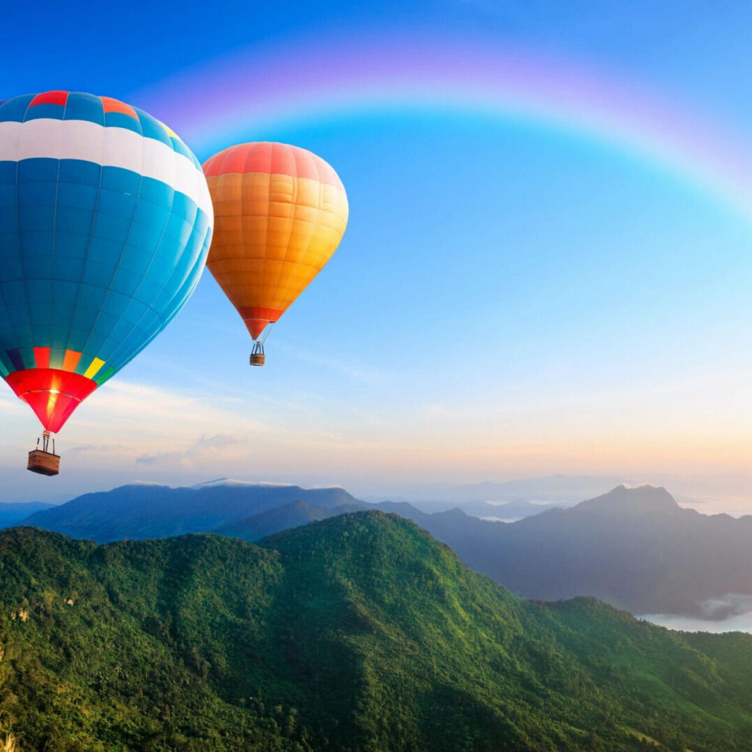 Two hot air balloons flying over a mountain range.