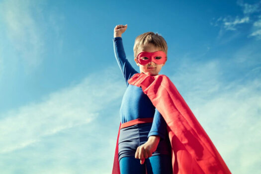 A young boy dressed as superman with his arm raised.
